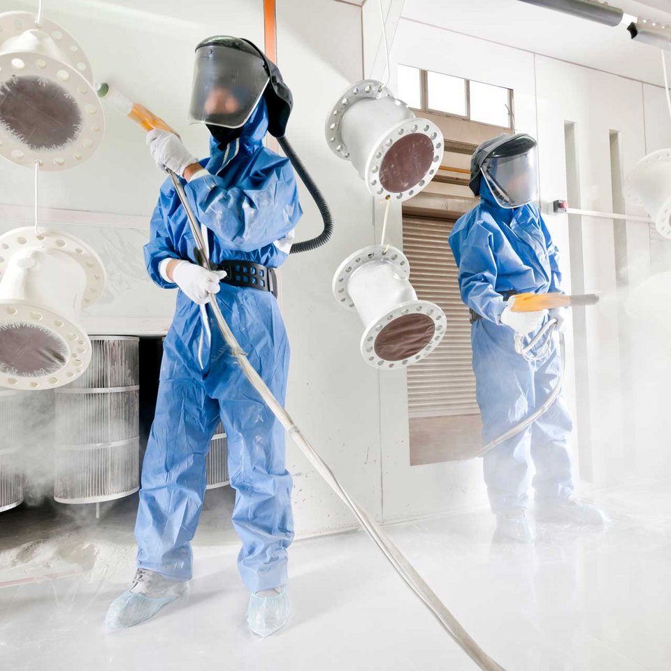 Zwei Mitarbeiter von Schmid Metallbearbeitung in Schutzanzügen beim Pulverbeschichten von Bauteilen